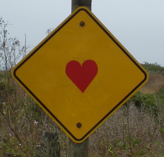 a yellow street sign with a red heart on it