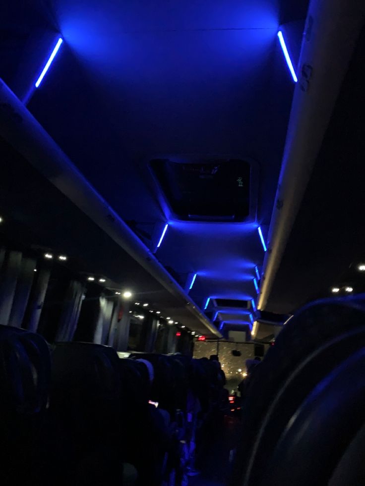 the inside of a bus with blue lights on it's ceiling and black seats