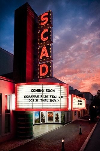 a movie theater sign lit up at night with the sun setting in the sky behind it