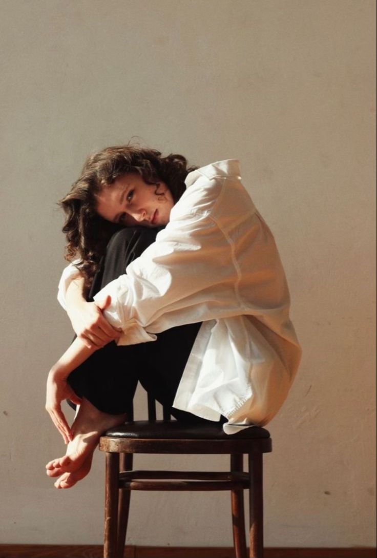 a woman sitting on top of a wooden chair with her arms around another person's head