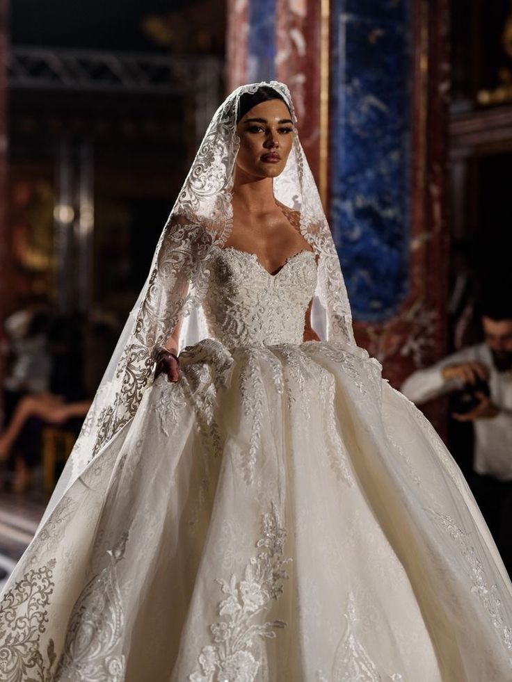 a model walks down the runway in a white wedding dress with long sleeves and a veil