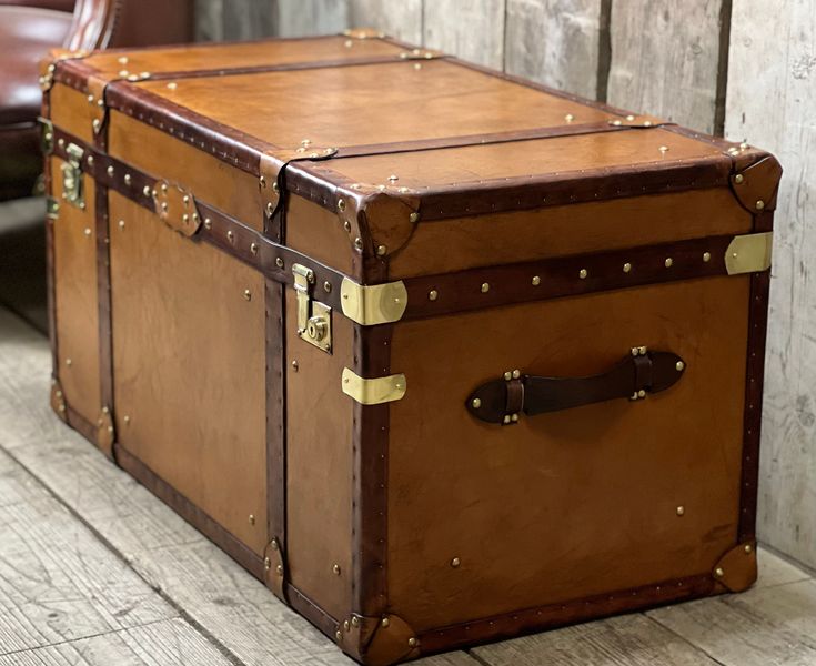 an old trunk is sitting on the floor next to a leather chair and wooden planks