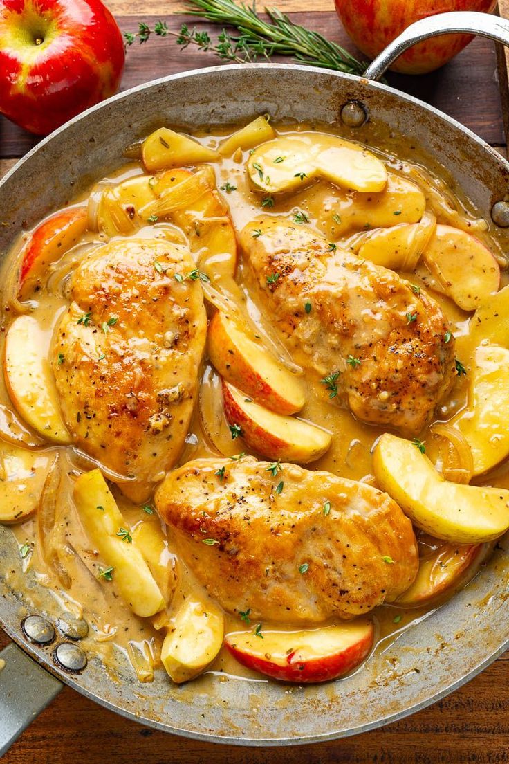 chicken with apples and potatoes in a skillet on a wooden table next to an apple