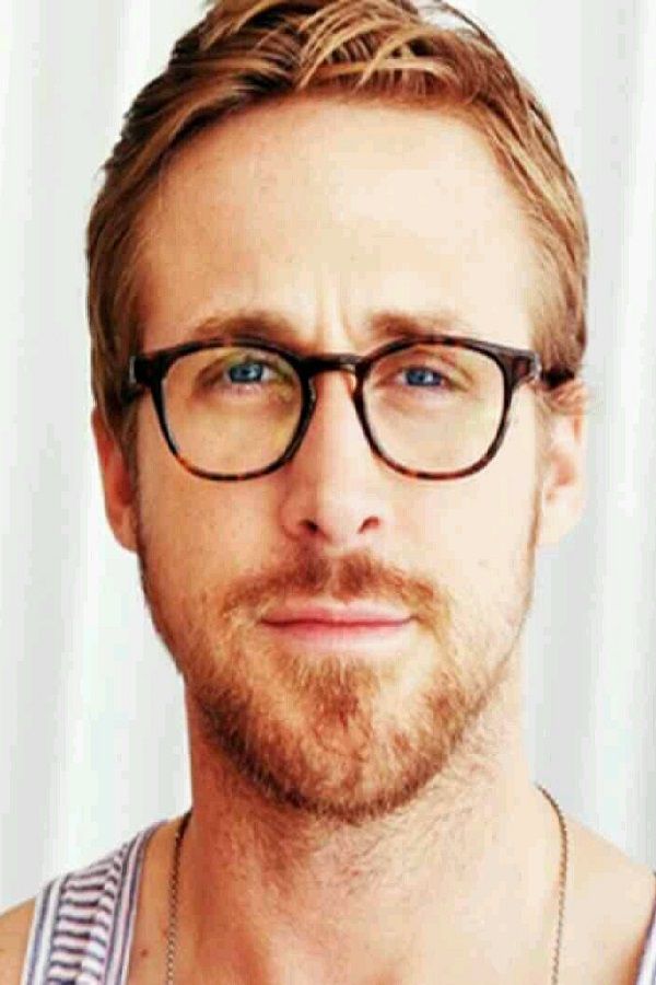 a man with glasses and a beard is posing for a photo in front of a white curtain