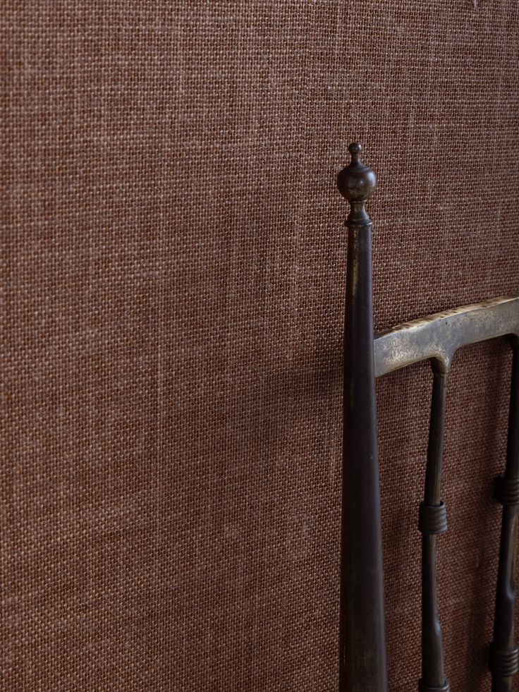 an iron bed headboard and foot board against a brown fabric wall with metal handrails