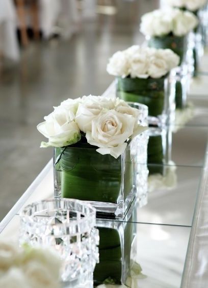 there are many vases with flowers in them on the long table, along with candles