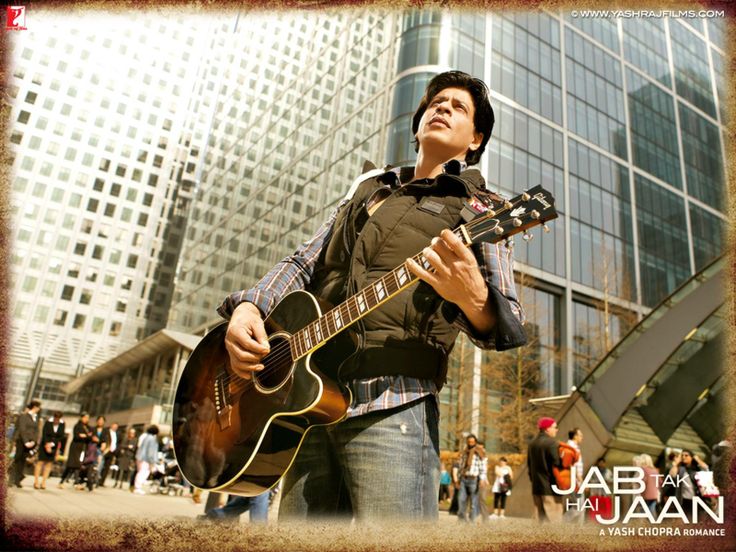 a man playing an electric guitar in front of tall buildings