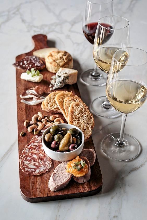 several wine glasses and some food on a wooden board