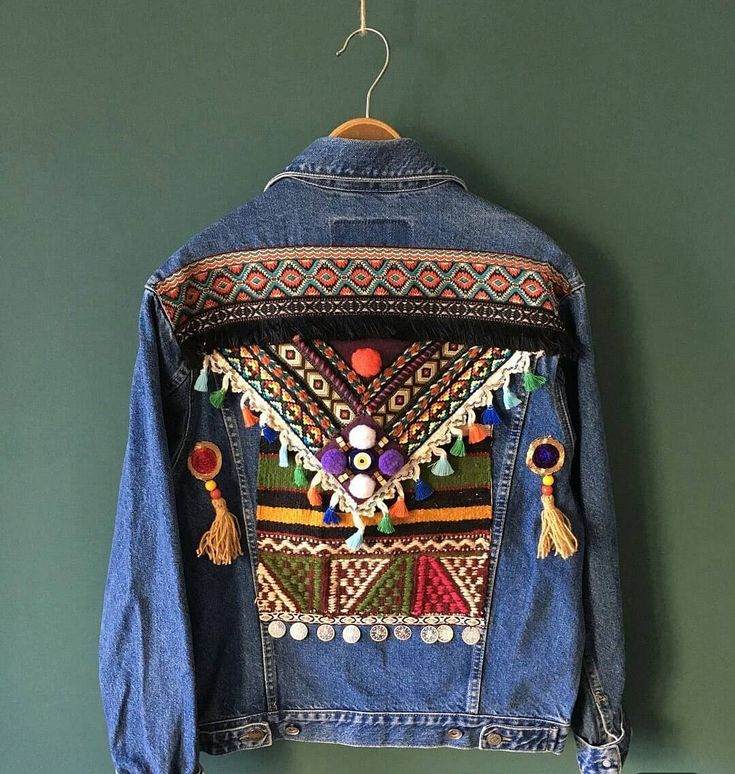 a denim jacket with embroidered details hanging on a green wall next to a coat hanger