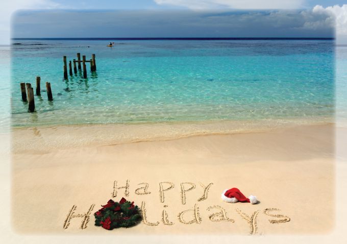 happy holidays written in the sand on a beach with santa's hat and presents