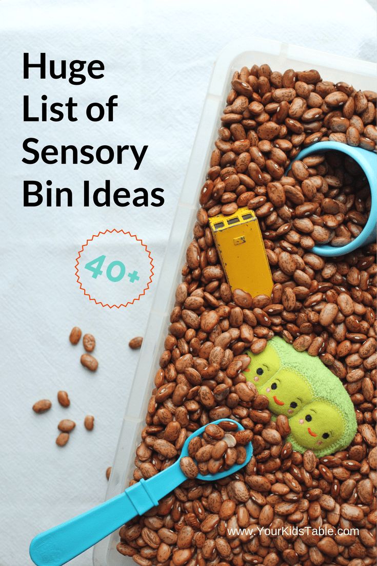 a bin filled with lots of brown beans and toys on top of it next to a blue pair of scissors