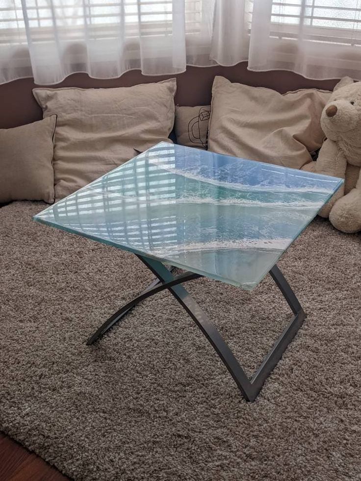 a glass coffee table sitting on top of a carpeted floor next to a teddy bear