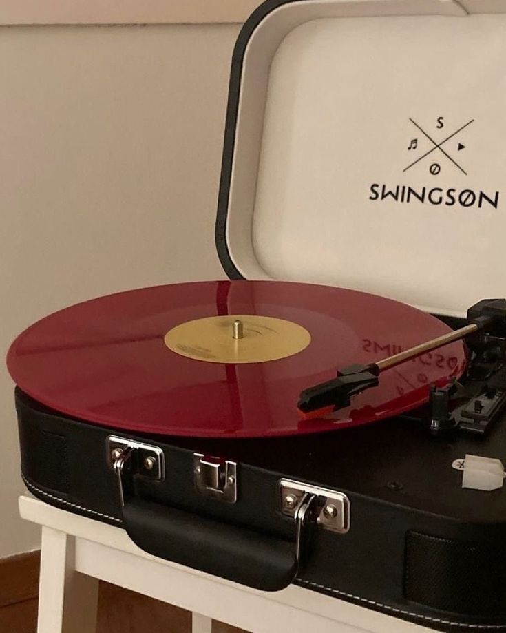 a red and black record player sitting on top of a white table next to a suitcase