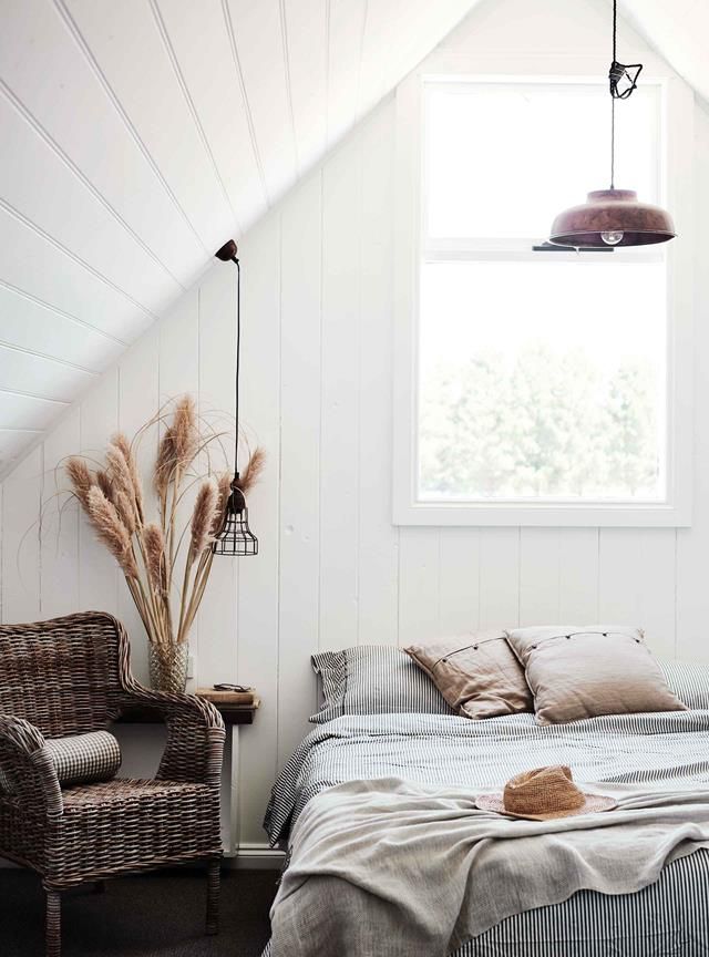 a bed sitting under a window in a bedroom next to a wicker chair and lamp