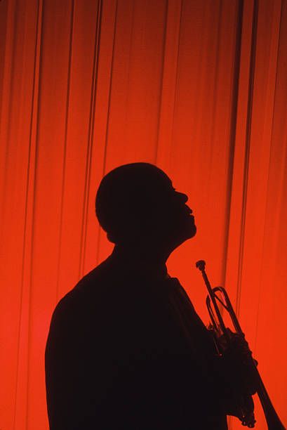 a man standing in front of a red curtain holding a trumpet