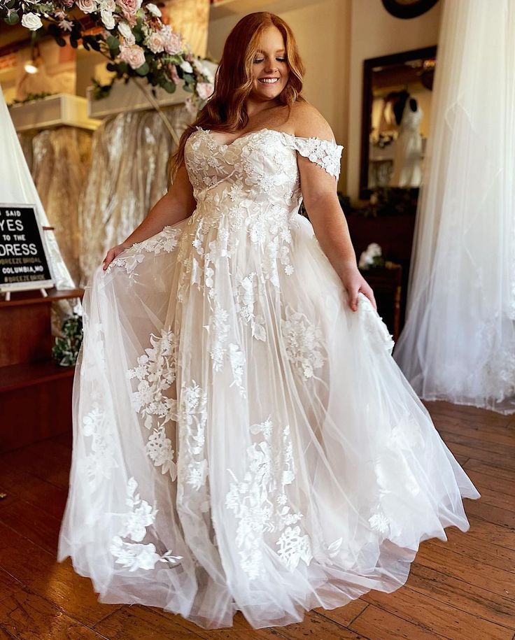 a woman in a white dress standing on a wooden floor with flowers hanging from the ceiling