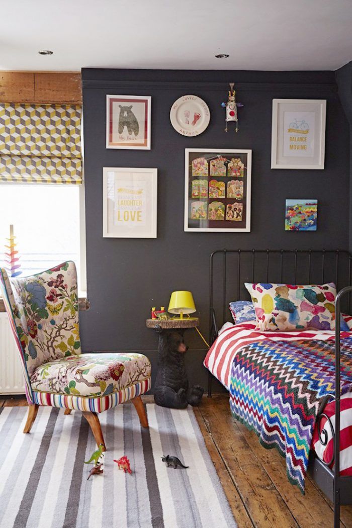 a dog sitting on the floor in front of a bedroom with black walls and colorful furniture