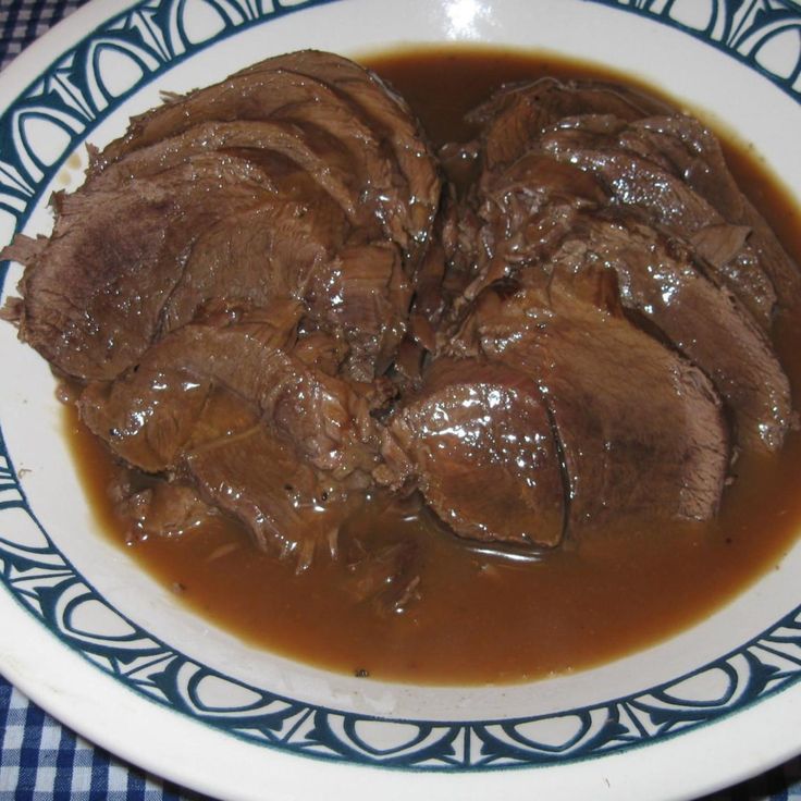 a white plate topped with meat and gravy on top of a blue checkered table cloth