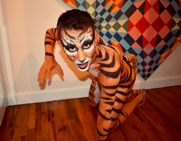 a young boy dressed as a tiger in front of a wall with an art work behind him