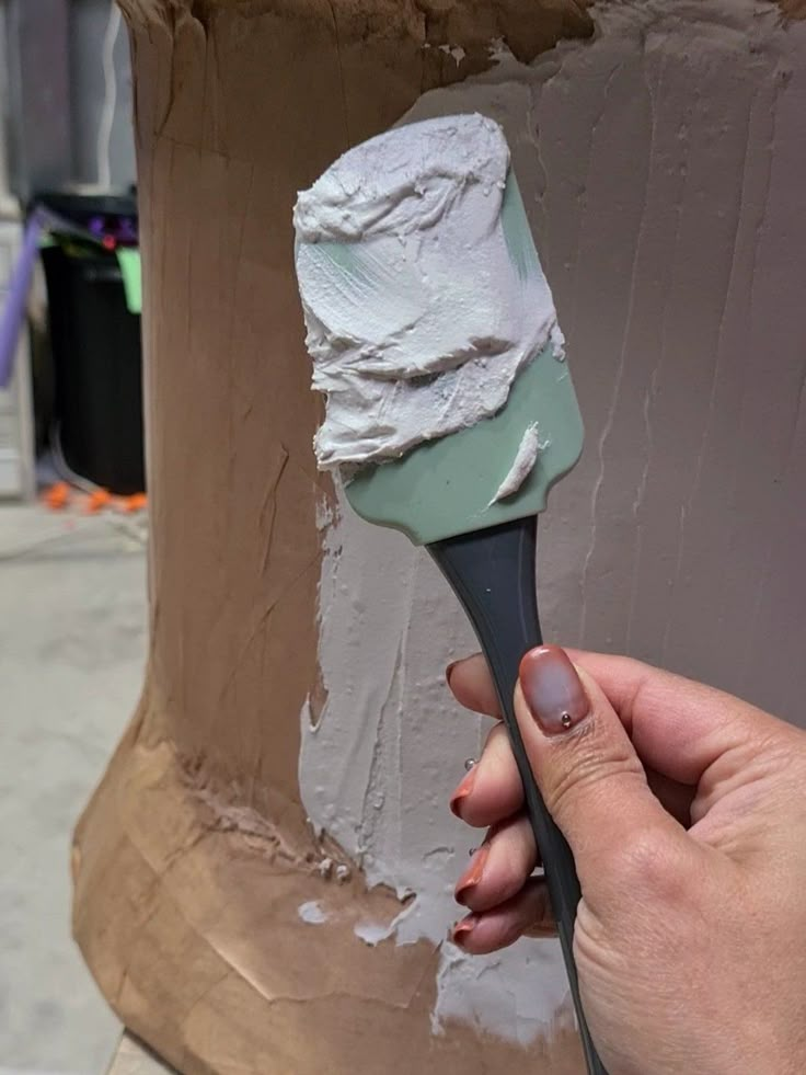 a hand holding a paintbrush in front of a painted pillar with white icing on it