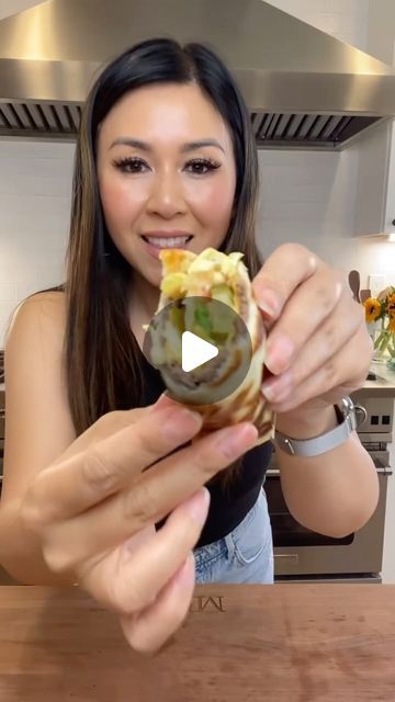 a woman holding up a piece of food in front of her face and smiling at the camera