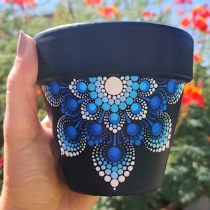 a hand holding a black cup with blue and white designs on the outside, in front of red flowers