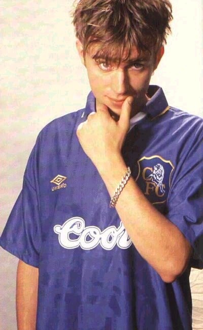 a young man posing with his hand on his chin and looking at the camera while wearing a blue shirt