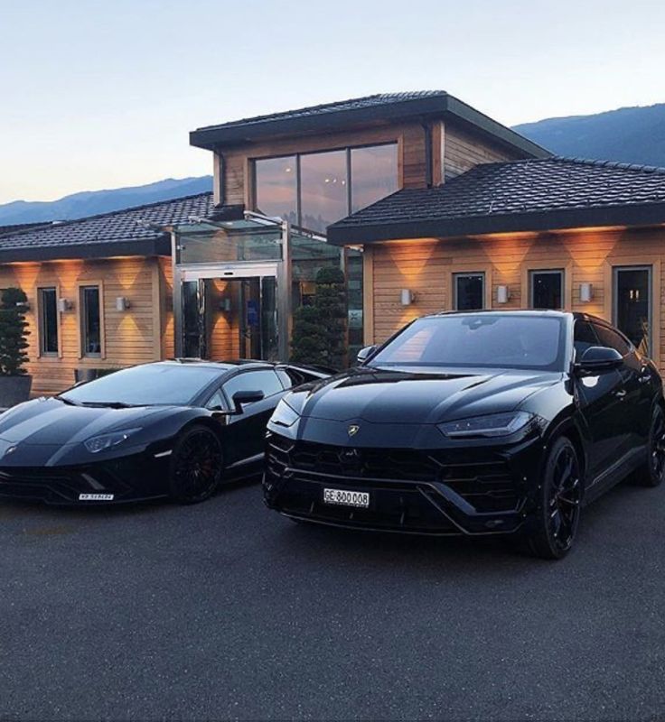 two black sports cars are parked in front of a house with mountains in the background