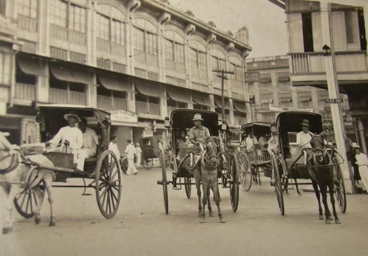 an old black and white photo of people riding in horse drawn carriages down the street