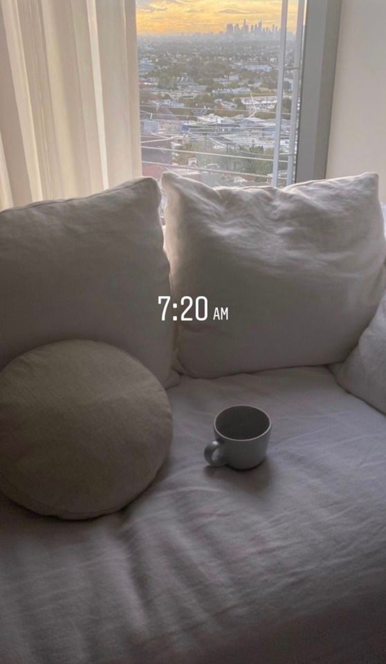 a coffee cup sitting on top of a white couch next to pillows and a window