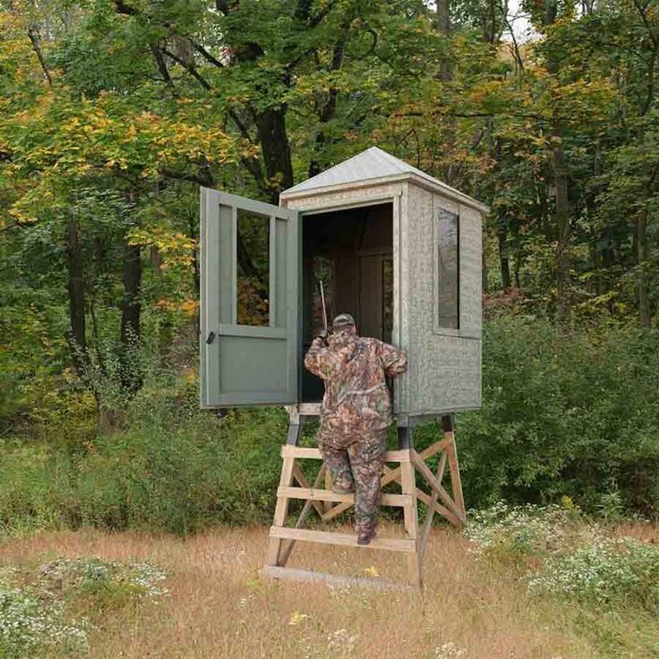 a man in camouflage standing at the door of a small outhouse