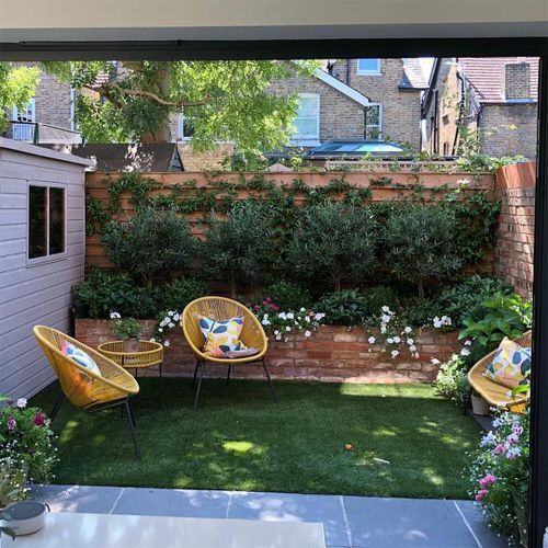 an outdoor area with chairs and flowers on the grass in front of a brick wall