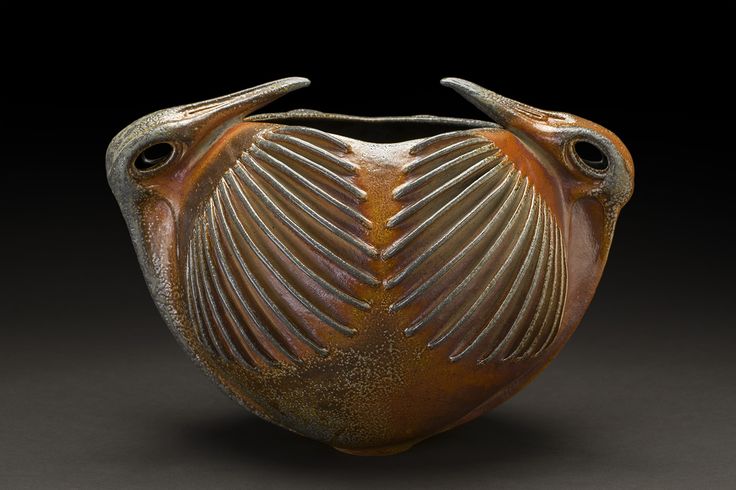 a brown vase sitting on top of a table next to a black background with two birds perched on it