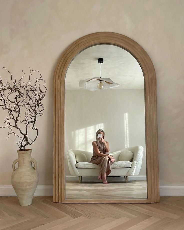 a woman sitting on a couch in front of a large mirror with a vase next to it