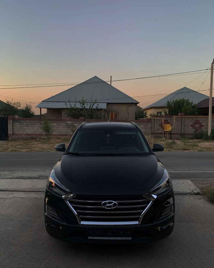 the front end of a black car parked in a parking lot next to some houses