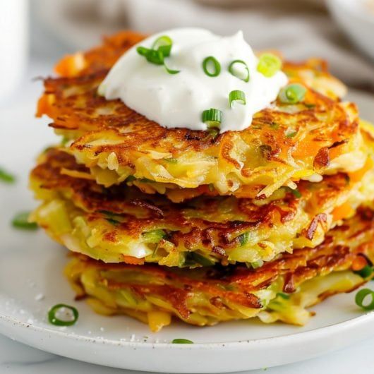 a stack of pancakes with sour cream on top and green onions in the middle, sitting on a white plate