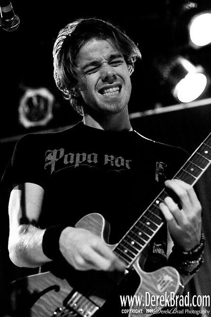 black and white photograph of a man playing guitar at a concert with microphone in the background