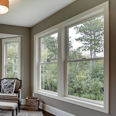 a living room filled with lots of windows next to a chair and ottoman on top of a hard wood floor