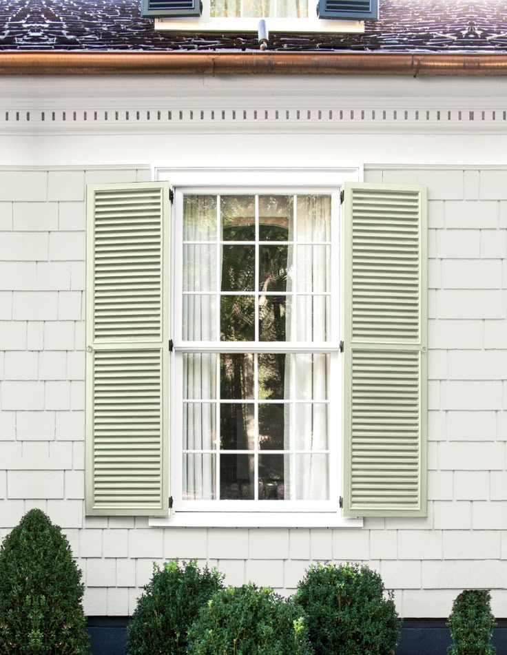 an open window with green shutters in front of a white house