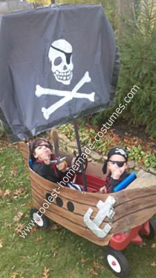 two children in a pirate boat costume with a black sail and skull on the side