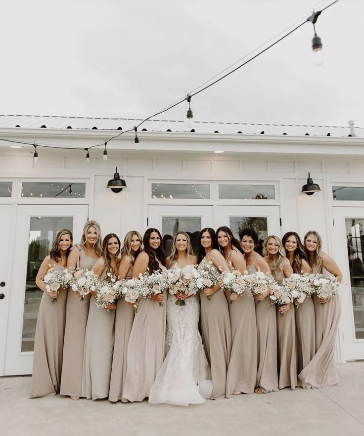 a group of women standing next to each other in front of a white building holding bouquets