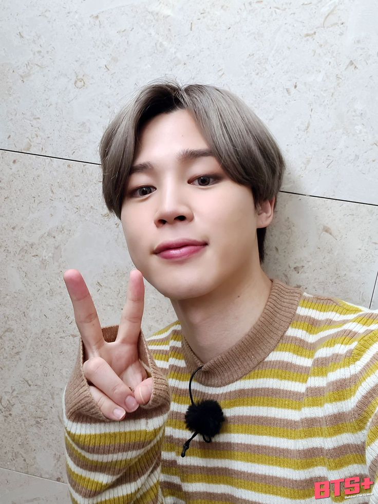 a young man making the peace sign with his hand while standing in front of a wall