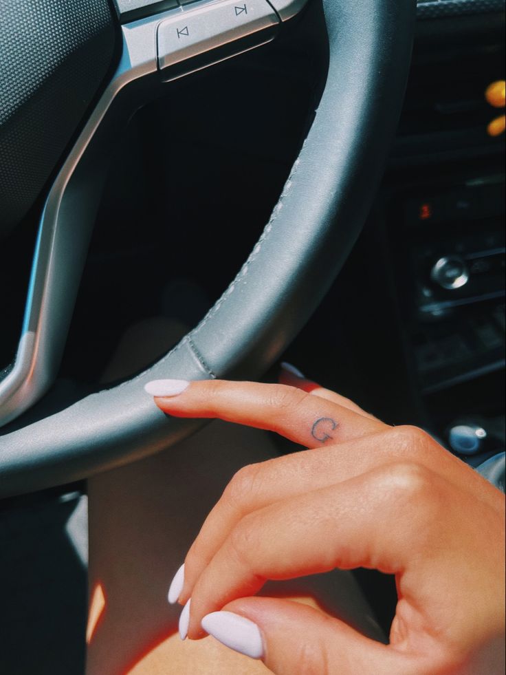 a woman's hand on the steering wheel of a car with a small tattoo