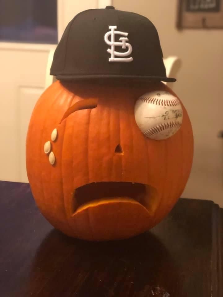 a baseball cap on top of a pumpkin with a face drawn in the shape of a ball