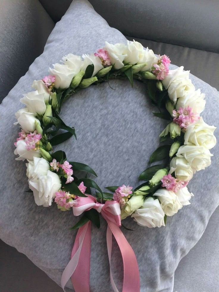 a wreath made out of flowers and pink ribbon on top of a gray couch cushion