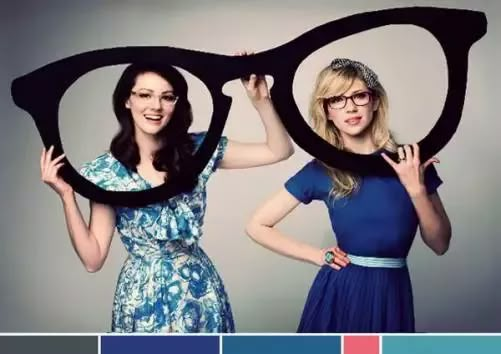 two women in blue dresses holding up large black eyeglasses with their hands and arms