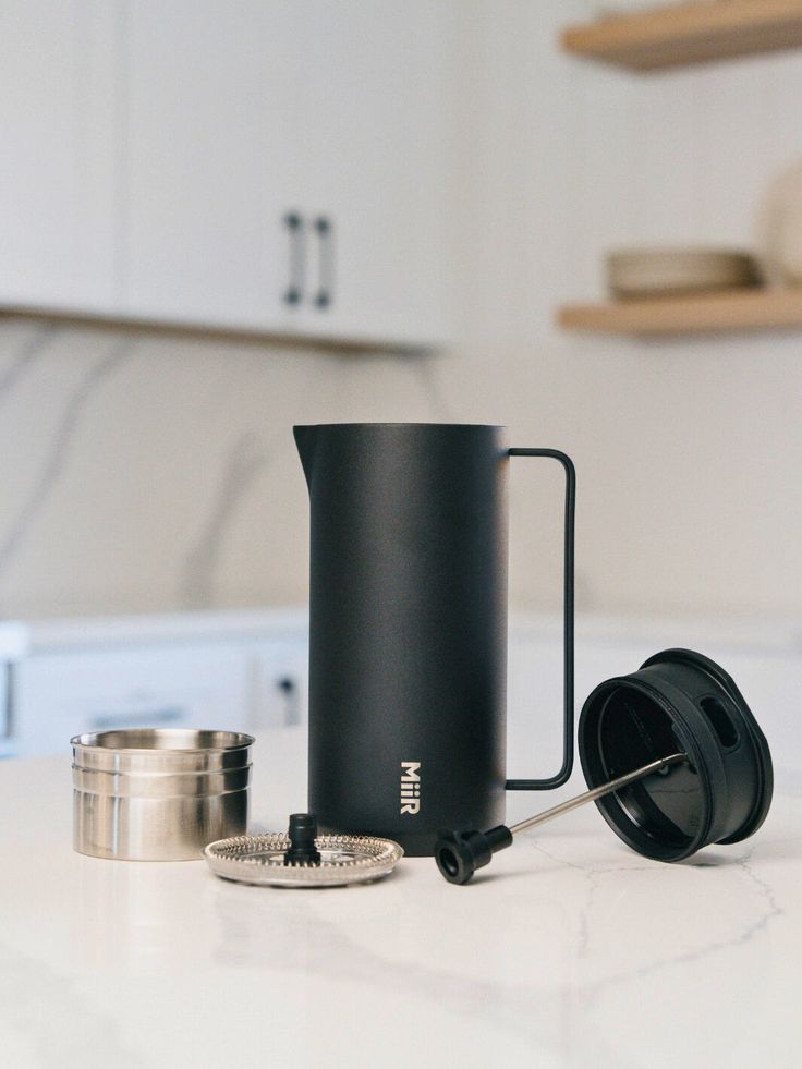 a black coffee pot sitting on top of a kitchen counter next to a measuring cup