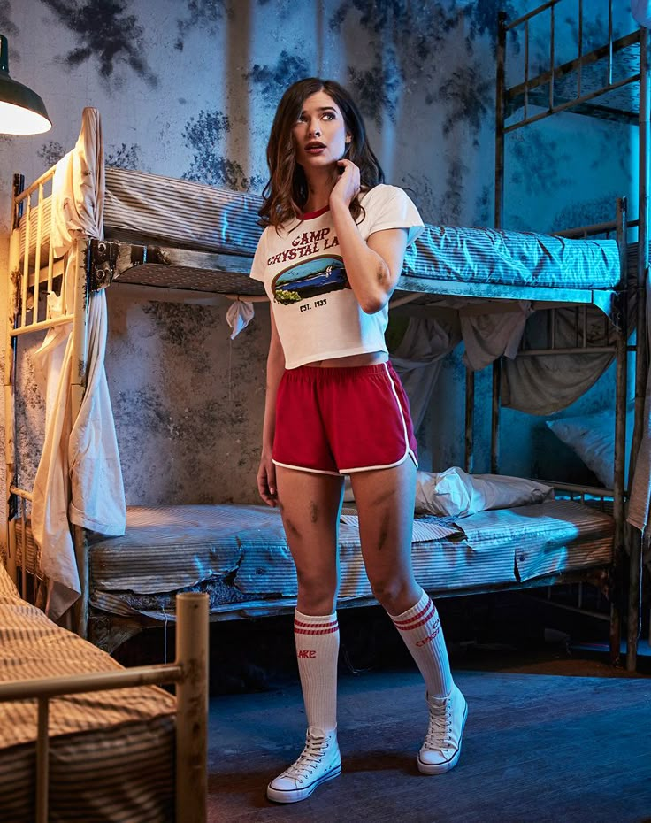 a woman standing in front of a bunk bed wearing red shorts and white shirt with her hand on her cheek