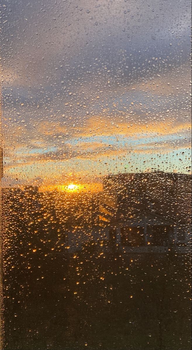 the sun is setting through rain drops on a window pane with buildings in the background