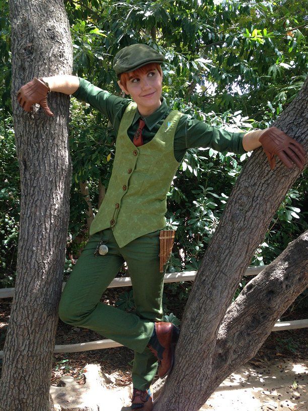 a man in green is leaning on a tree and posing for the camera with his arms stretched out